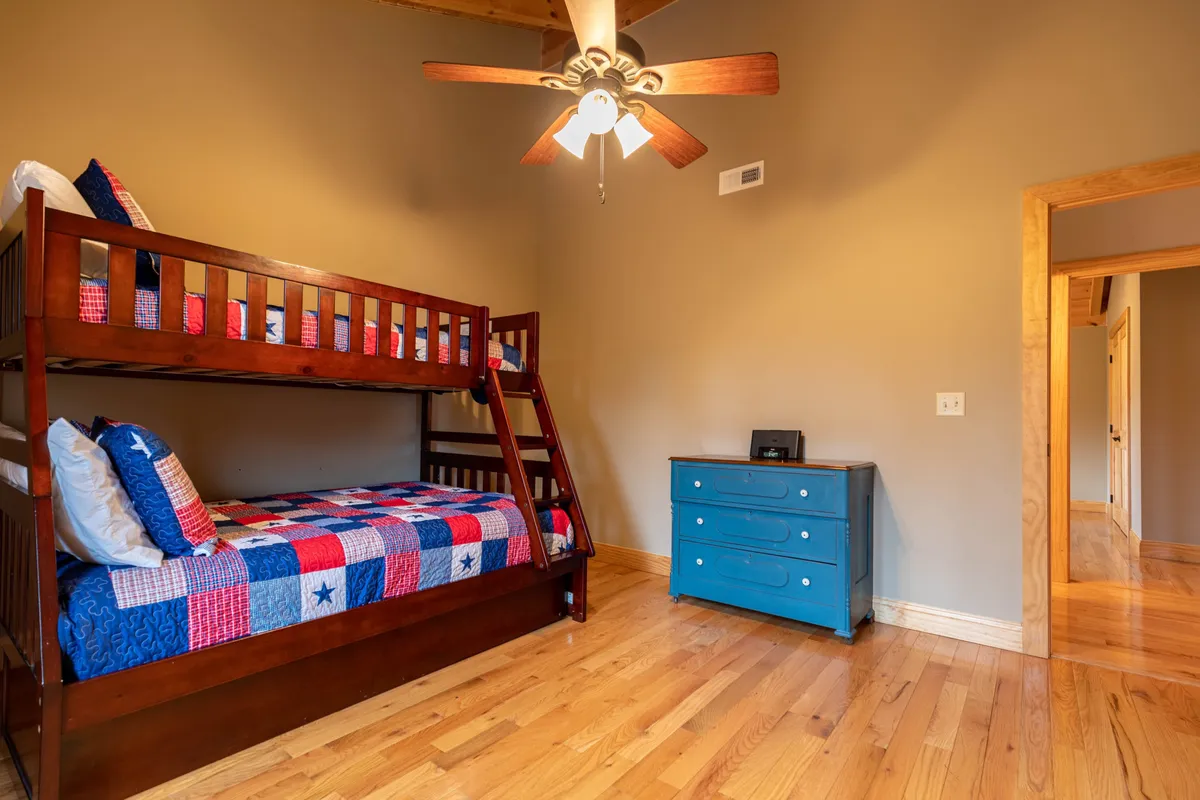 A cheerful bunk room with a sturdy wooden bunk bed, blue dresser, and ceiling fan, designed for kids to sleep, play, and make memories together.
