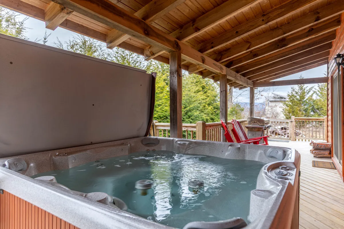 The image highlights the hot tub area on a wooden deck, surrounded by nature and outfitted with red chairs. The tranquil atmosphere is complemented by beautiful mountain views, making this a spot to soak and connect with the scenic outdoors morning or evening.