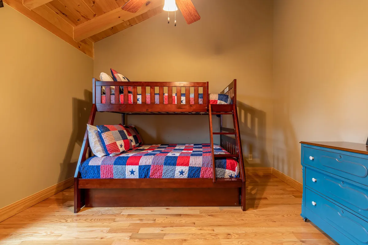 An inviting interior scene featuring a bunk bed and a blue dresser under a wooden ceiling. The space feels playful and cozy, perfect for kids to build forts, read, or share late-night stories.