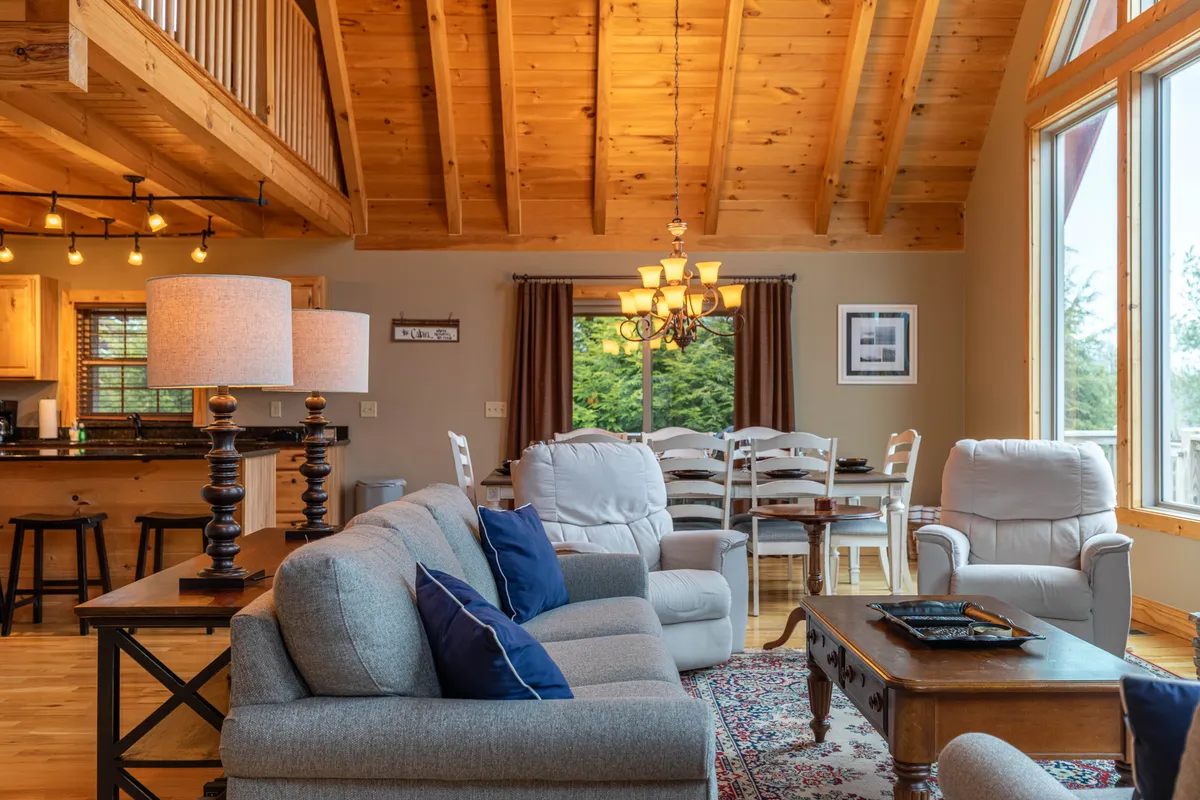 A warm, inviting interior scene featuring a comfortable sofa with cushions, a dining table set for eight, and large windows that offer views of the outdoors. The chandelier adds a touch of elegance, while the entire space radiates an atmosphere perfect for family gatherings.