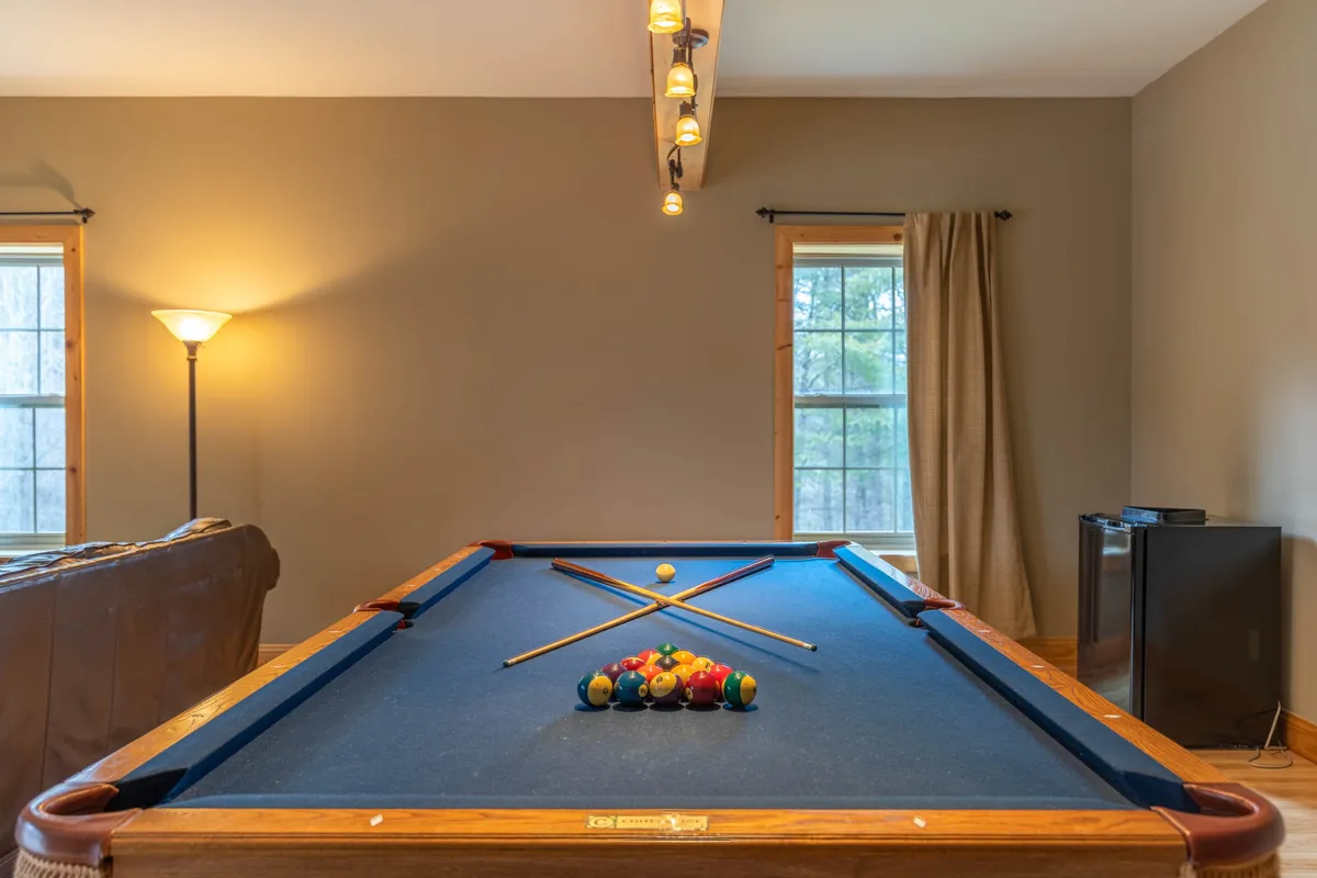 A fun-filled entertainment area with a pool table, cozy seating along the windows, and an inviting lighting fixture overhead. The windows provide glimpses of the outdoors, while the seating area encourages relaxed conversations and group activities.