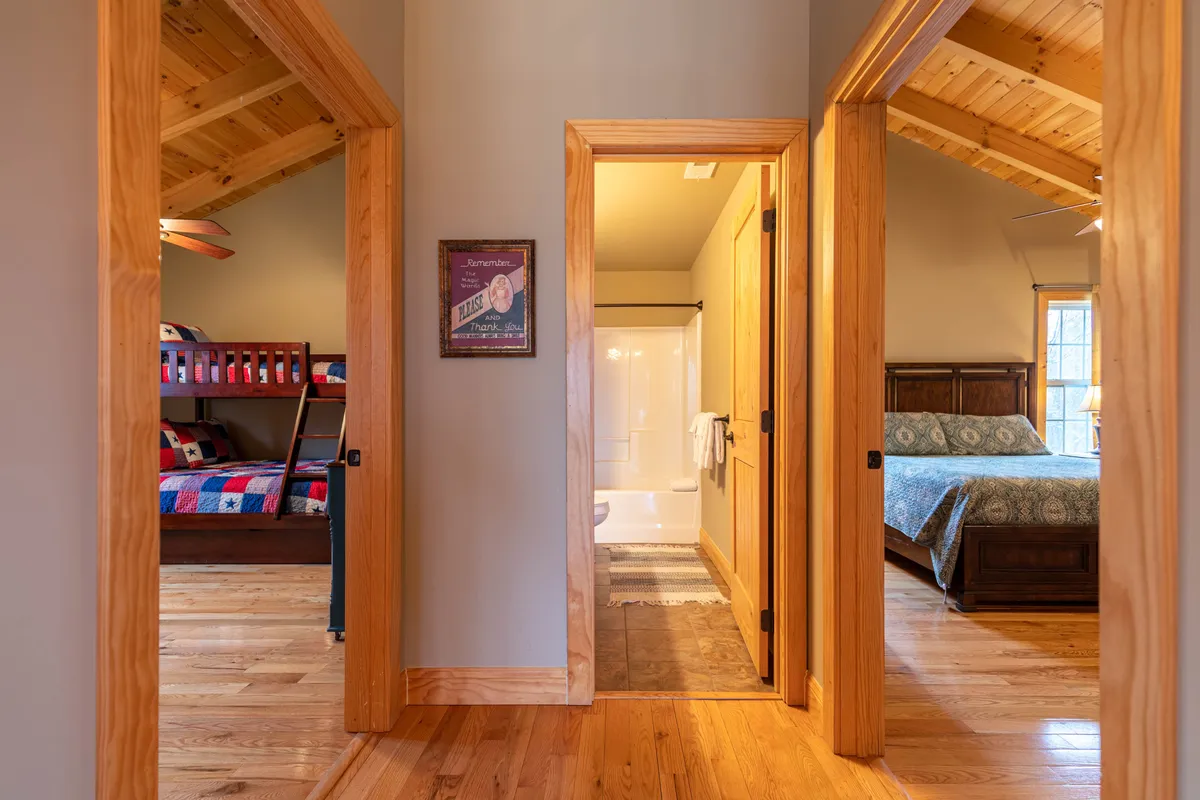 A warm and inviting bedroom that includes both a main bed and a bunk bed, with wooden beams, a bathroom entrance, and cheerful decorative wall art—suggesting a family-friendly space.