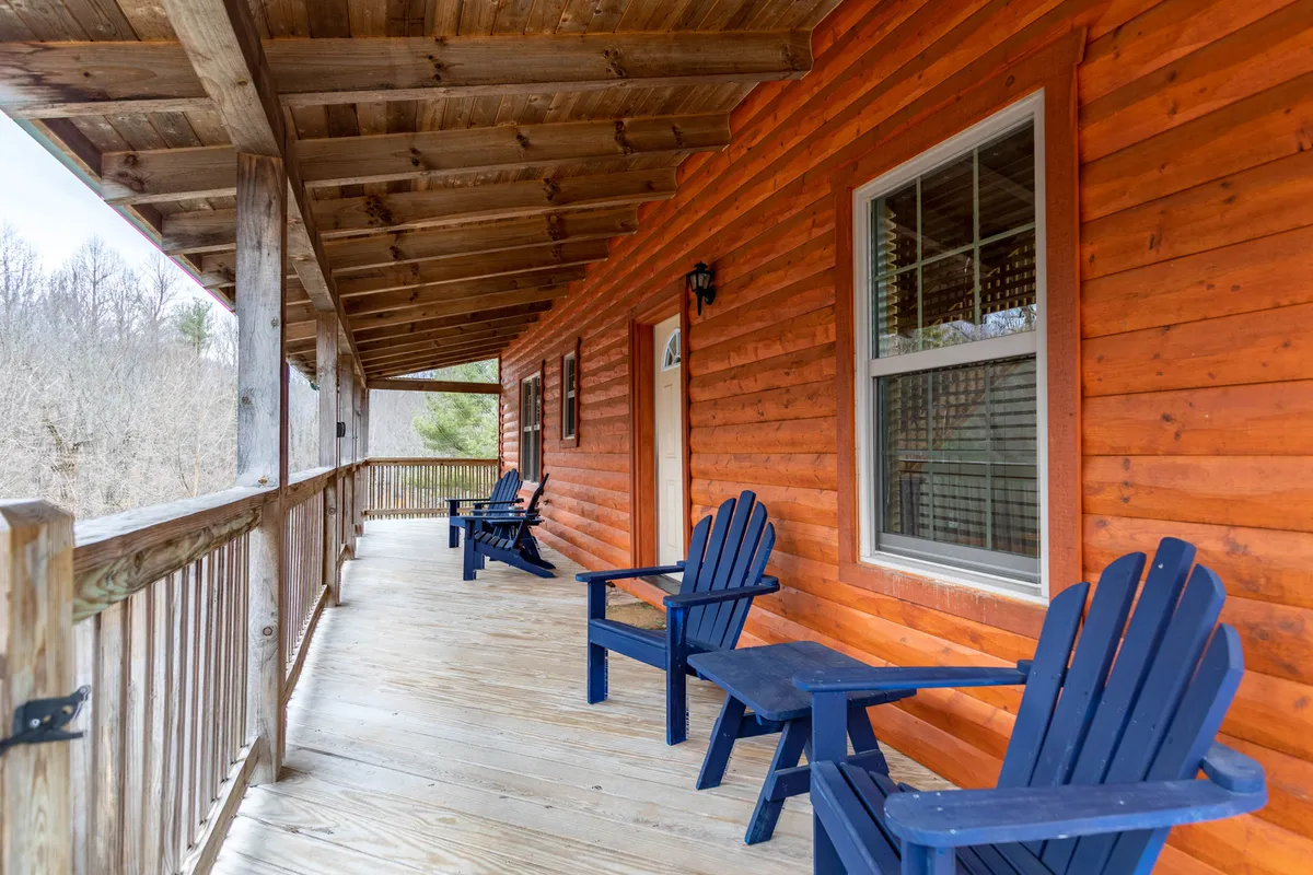 A serene exterior scene captures a wooden deck with blue chairs overlooking the natural surroundings, highlighting the cabin’s close connection to the outdoors. The log-style architecture and leafy backdrop create a peaceful place to enjoy coffee at sunrise or relax after hiking.