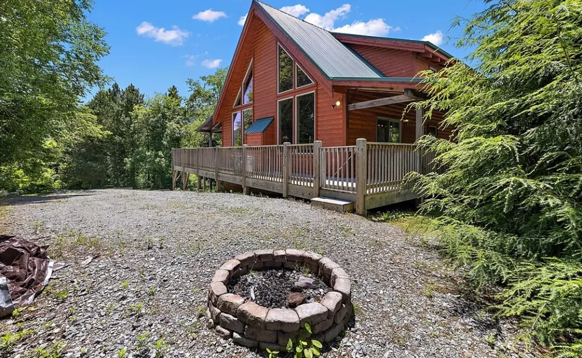 This image features the log cabin's exterior, highlighting a spacious deck and a central fire pit surrounded by inviting seating. The scene captures an atmosphere of relaxation and togetherness, with space for families to gather, barbecue, and share stories under open skies.
